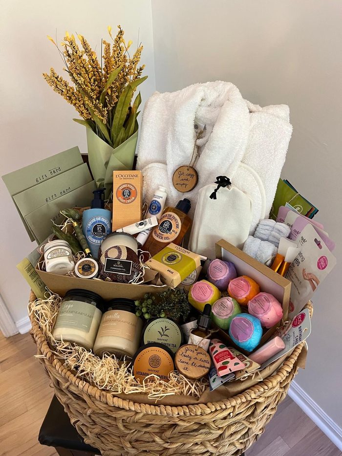 A large woven raffle basket filled with spa and self-care items: a plush robe, candles, bath bombs, lotions, face masks and gift cards