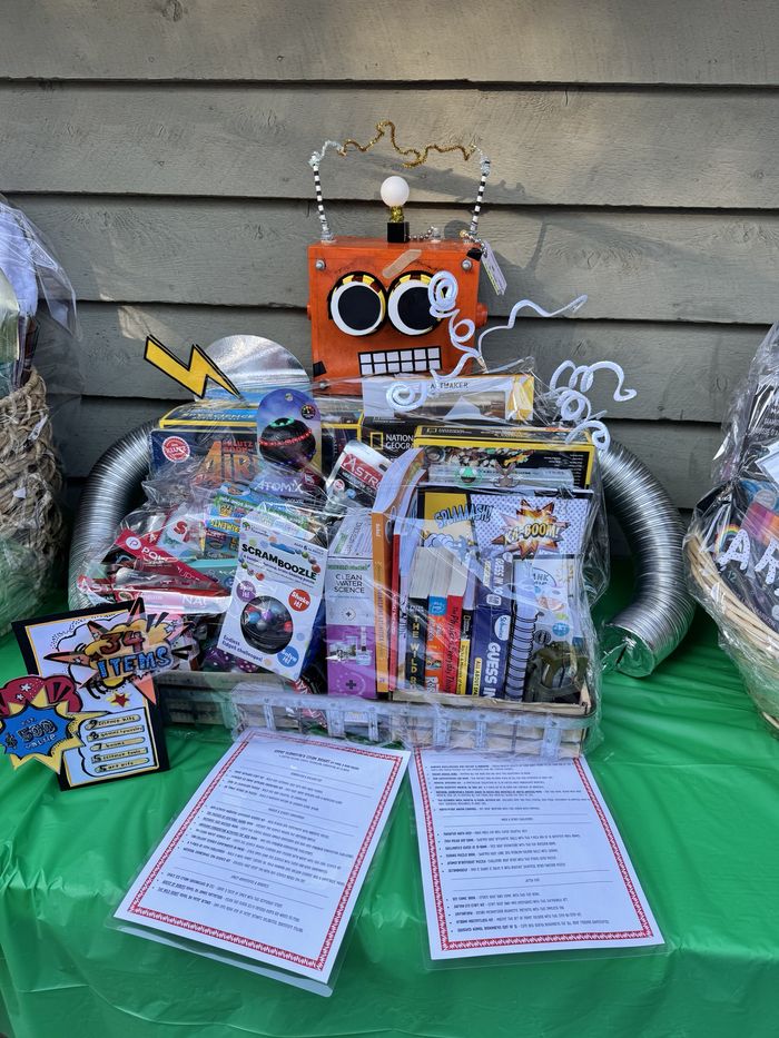 A STEM raffle basket topped with a handmade orange robot, packed with science kits, puzzles, books and art kits