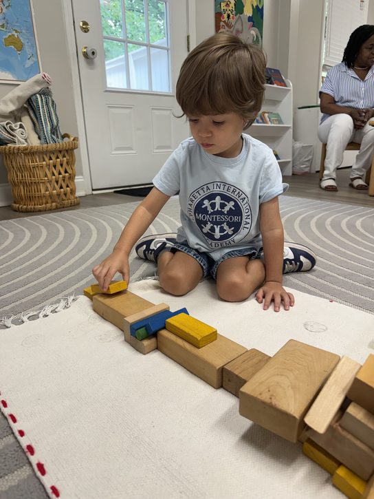 A Pre-Primary student placing wooden blocks on a work rug