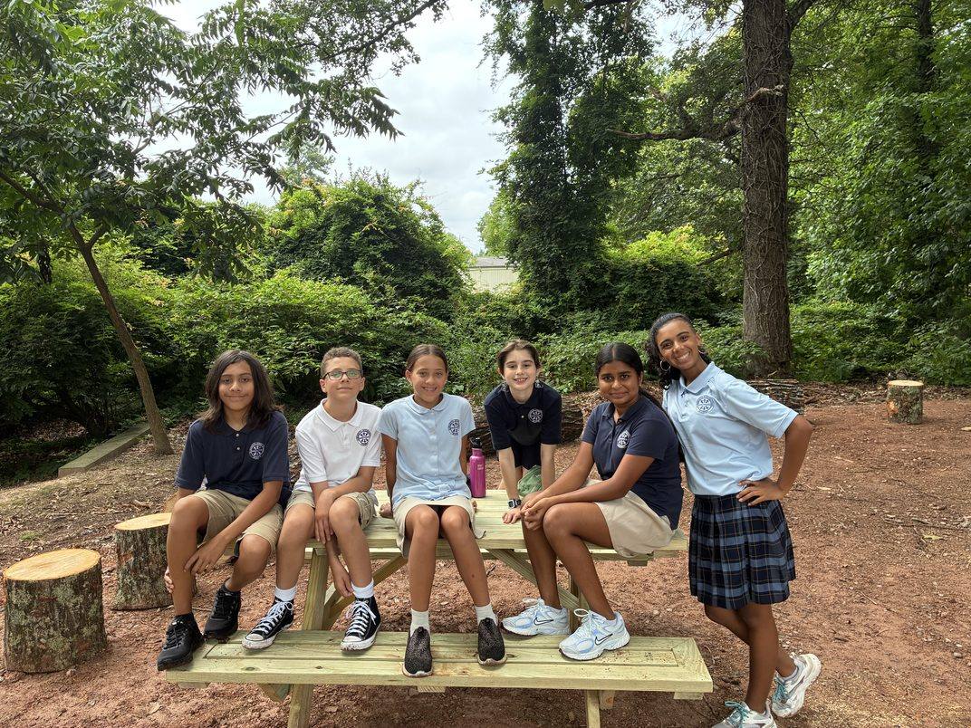 Six Middle School students seated together on the new picnic table in the outdoor gathering area
