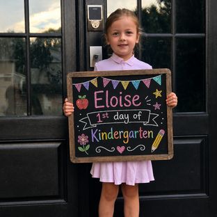 A student holding a first day of Kindergarten chalkboard