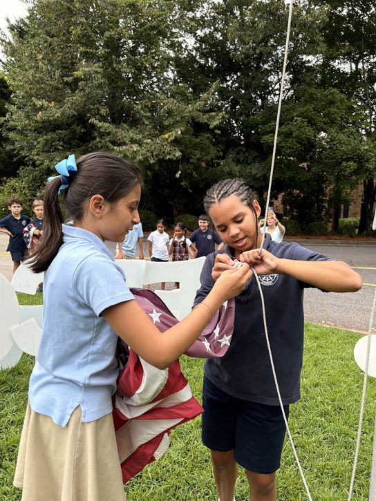 Two Upper Elementary students working together to raise the flag on the front lawn