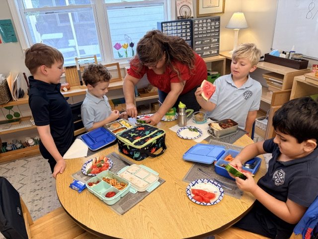 Lower Elementary students around a table sharing watermelon while their guide serves