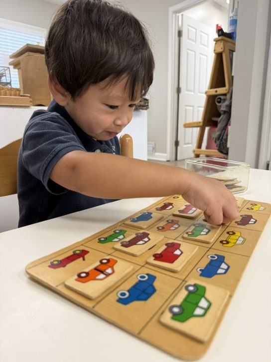 A young student placing matching vehicle tiles onto a wooden board