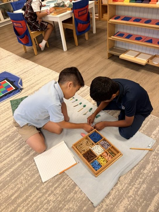 Two Elementary students kneeling over a box of bead bars, skip counting by twos together