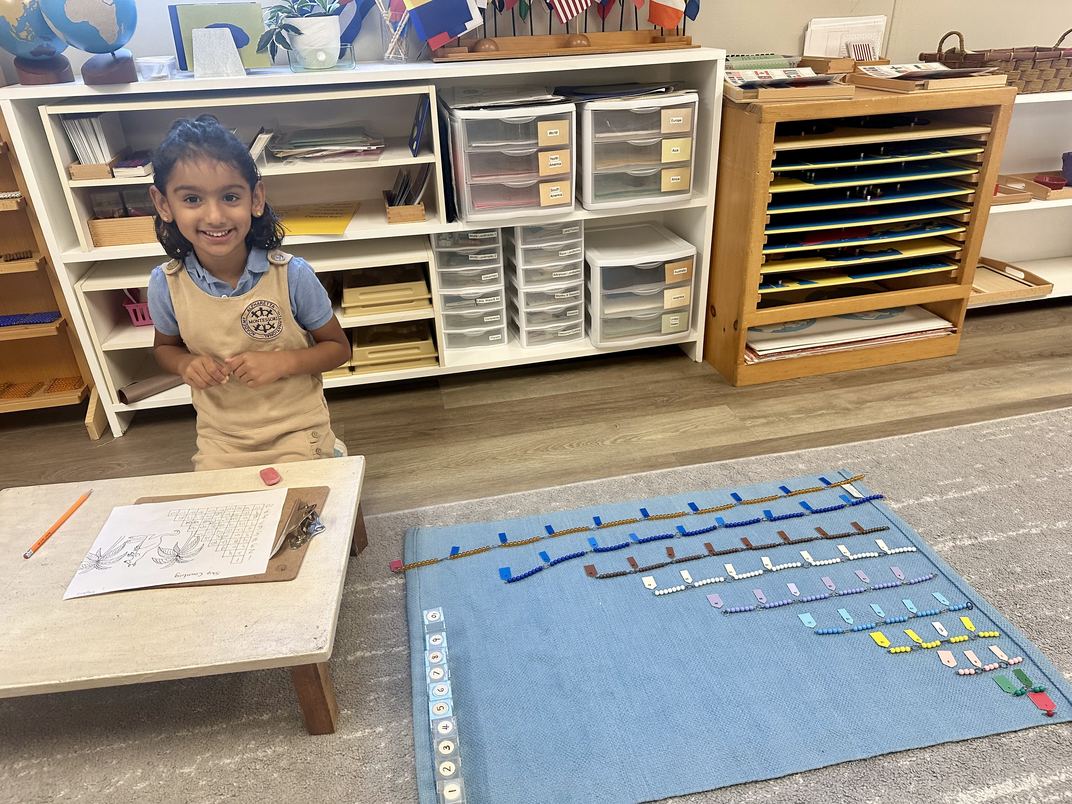 A Primary student beside a work rug laid out with skip counting bead chains and a recording sheet