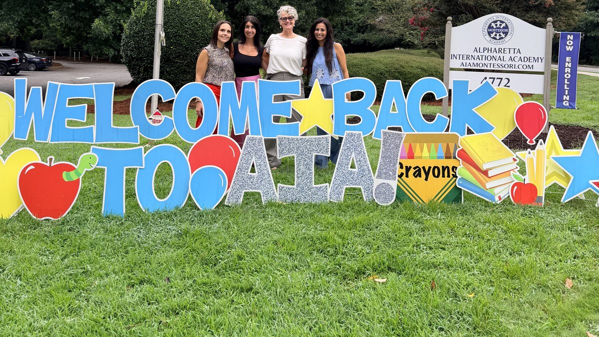 AIA staff welcoming families beside the Welcome Back to AIA sign on the first morning of school