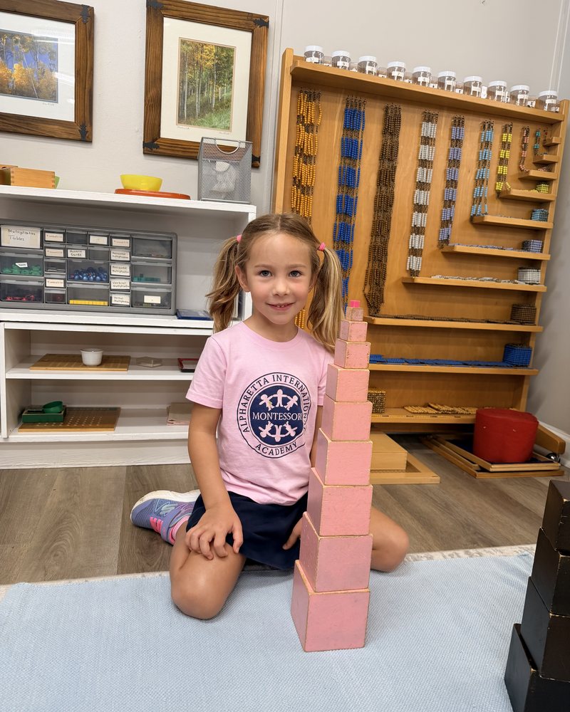 A Primary student kneeling beside a completed Pink Tower