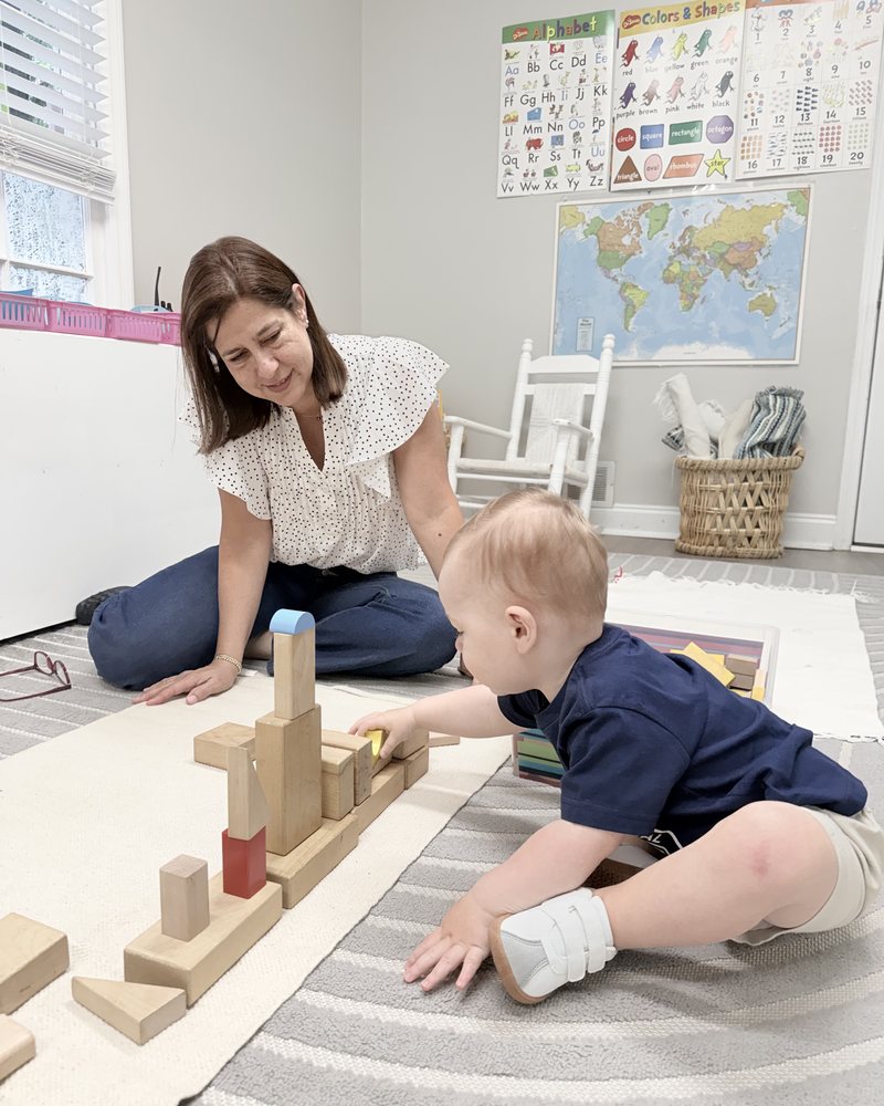 A guide sitting on the floor beside a toddler building with wooden blocks