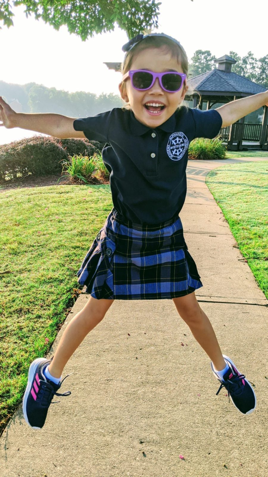 A young AIA student in uniform jumping for joy on the way to school