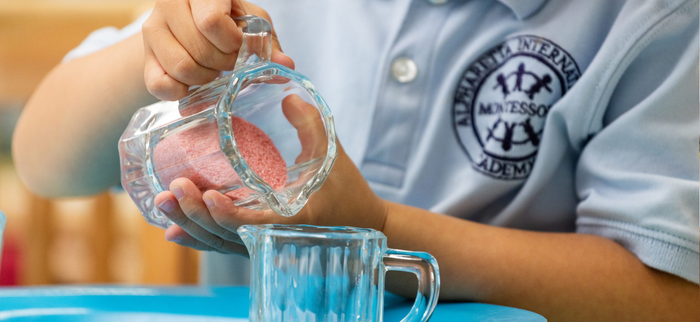 A child's hands pouring carefully between two glass pitchers during a practical life work