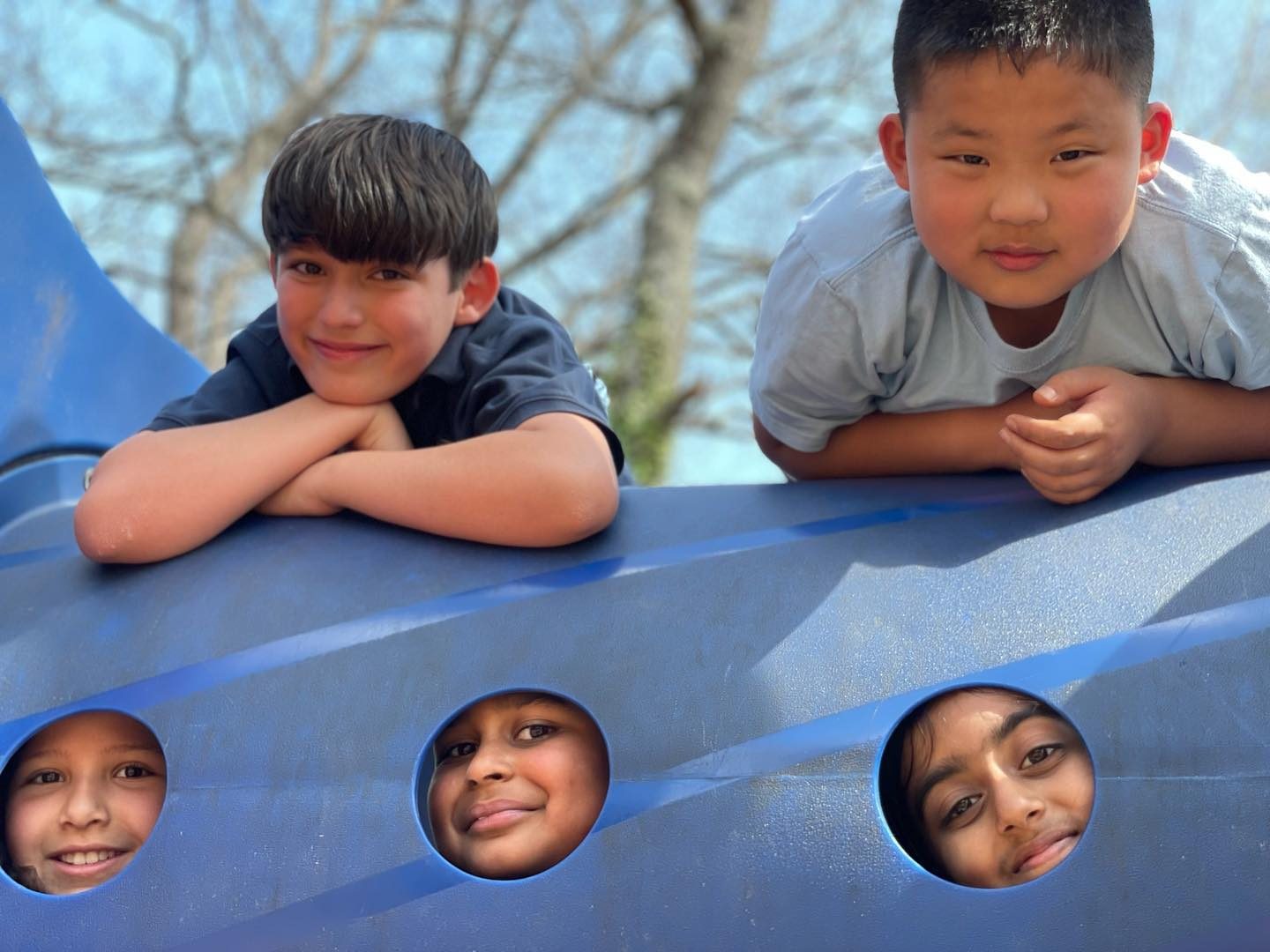 Five AIA students peeking through the playground climber, laughing