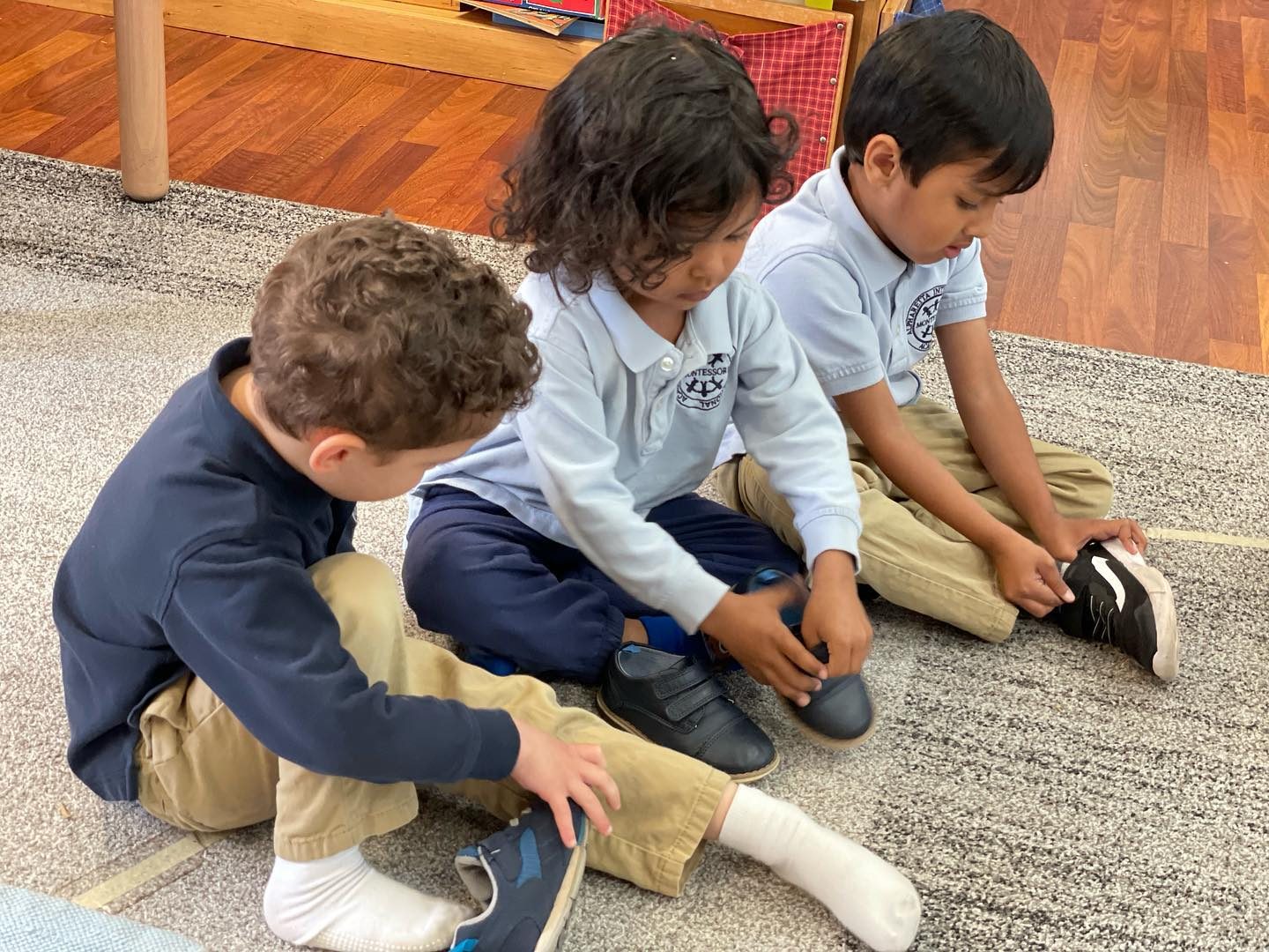 Three Pre-Primary students putting on their own shoes, side by side