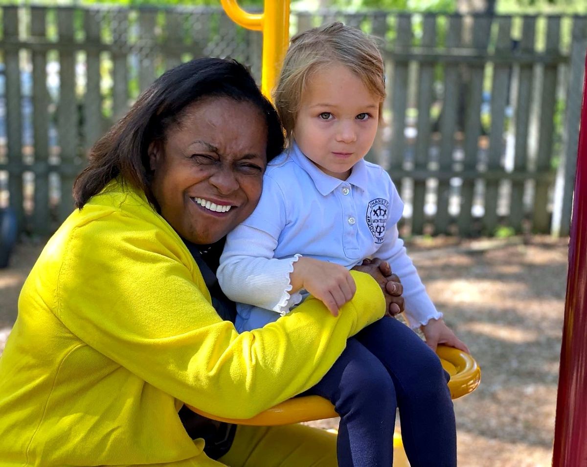 A Pre-Primary teacher warmly holding a toddler on the playground swing