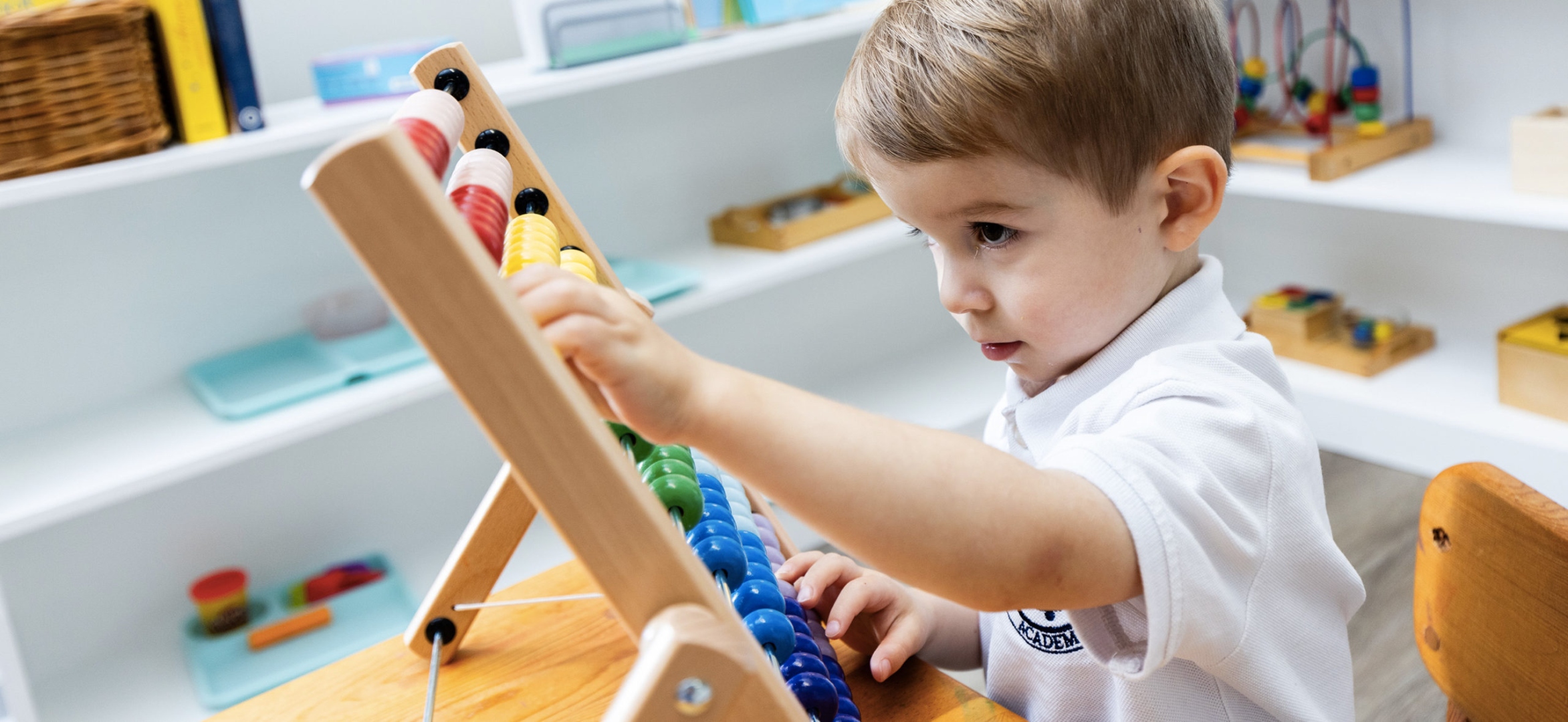 A young AIA student working with a colorful Montessori abacus, deep in focused hands-on math work