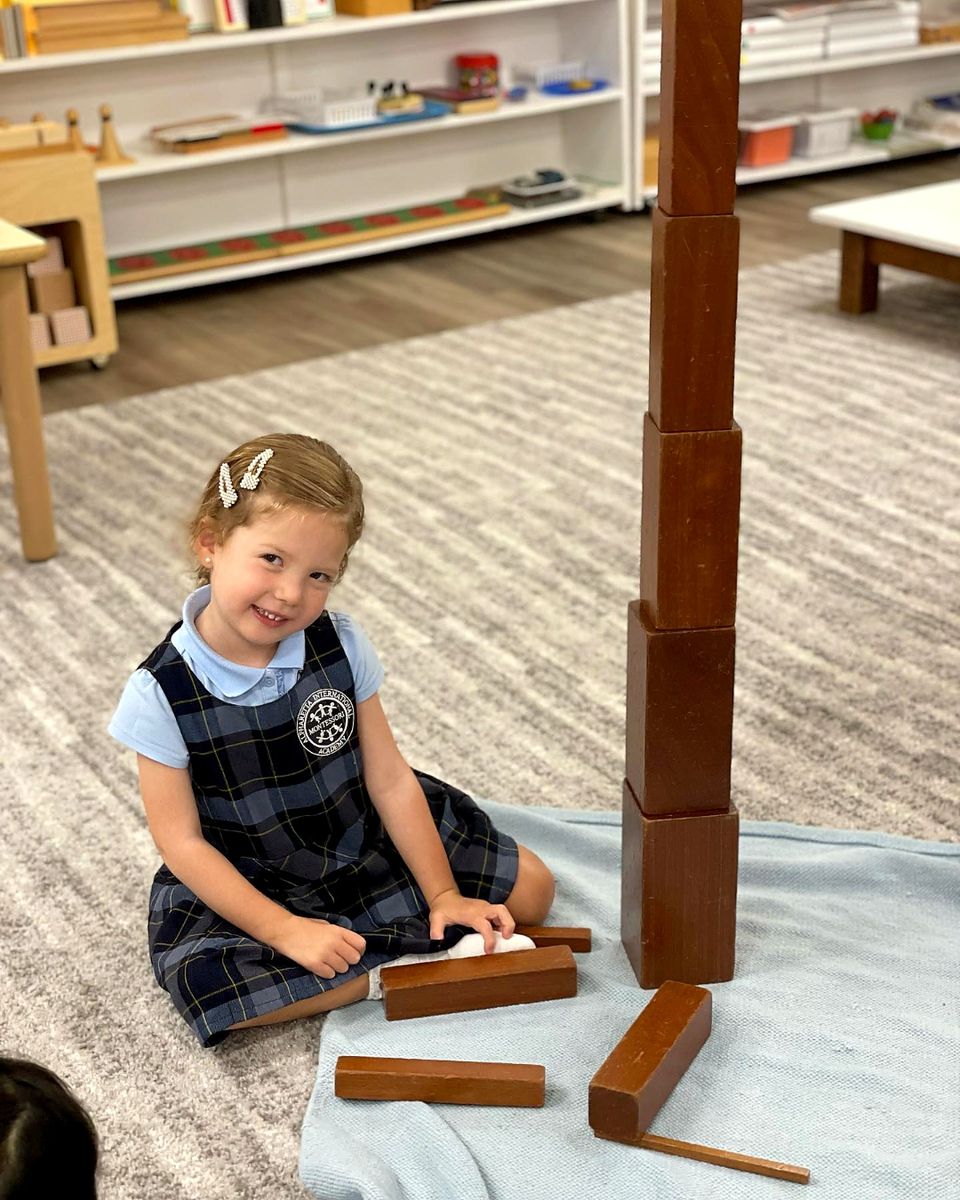 A Primary student smiling while working with the Brown Stair Montessori material
