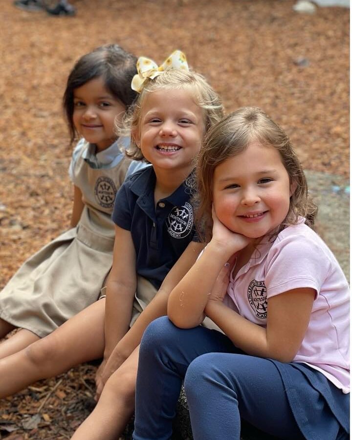 Three young AIA students sitting close together on the playground, smiling