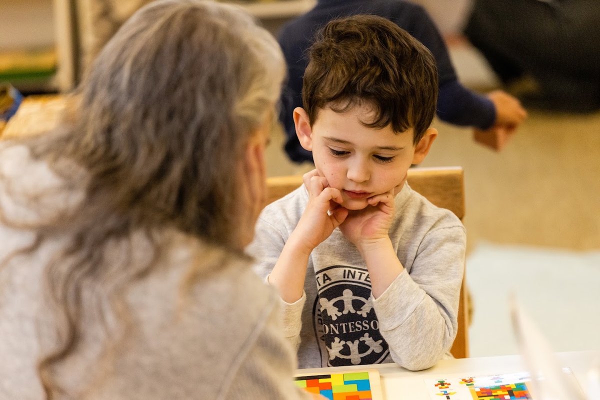 A Kindergarten-age student concentrating during a lesson with his guide at AIA Montessori