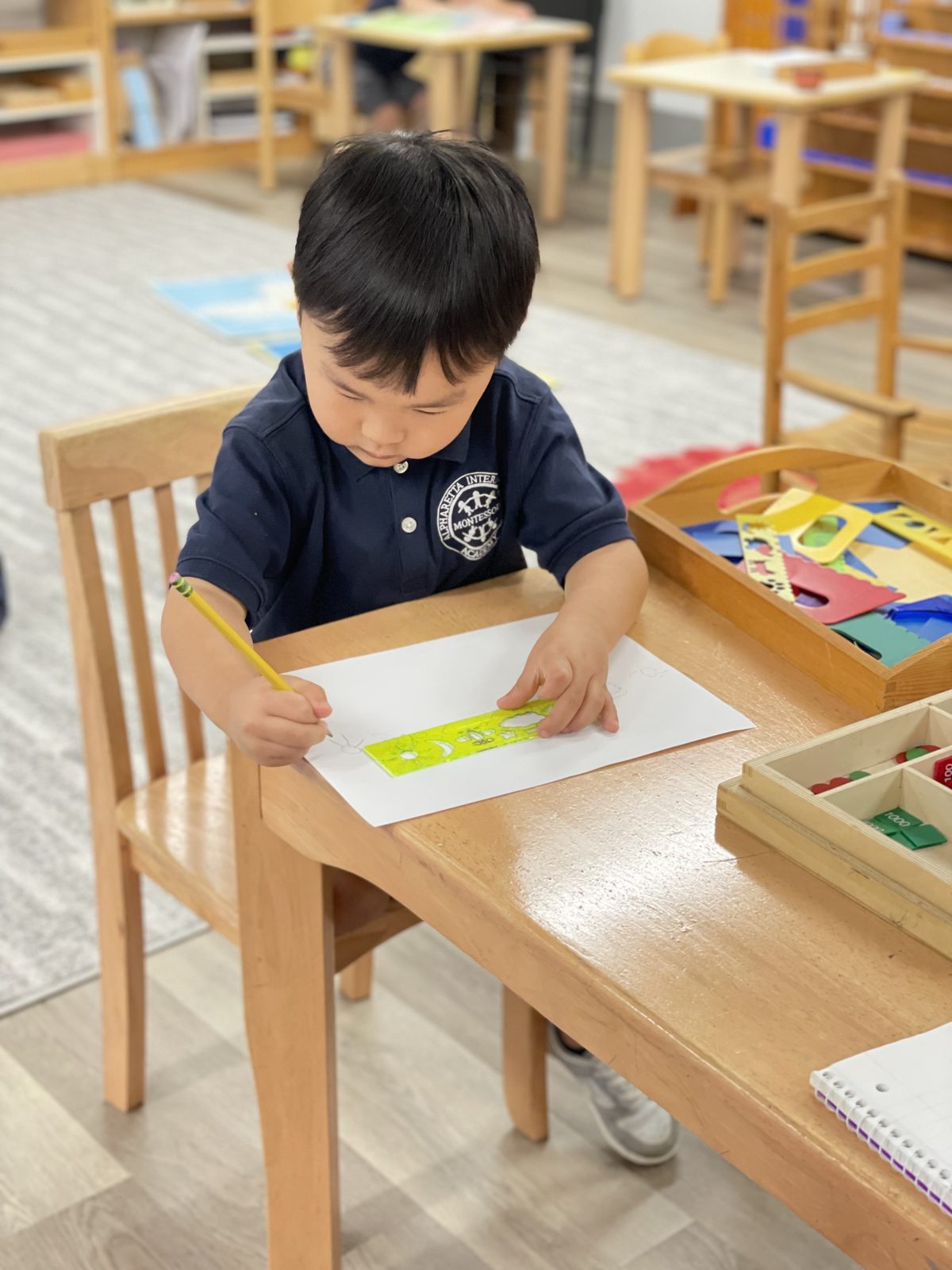 A Primary student tracing shapes with a stencil at a classroom table
