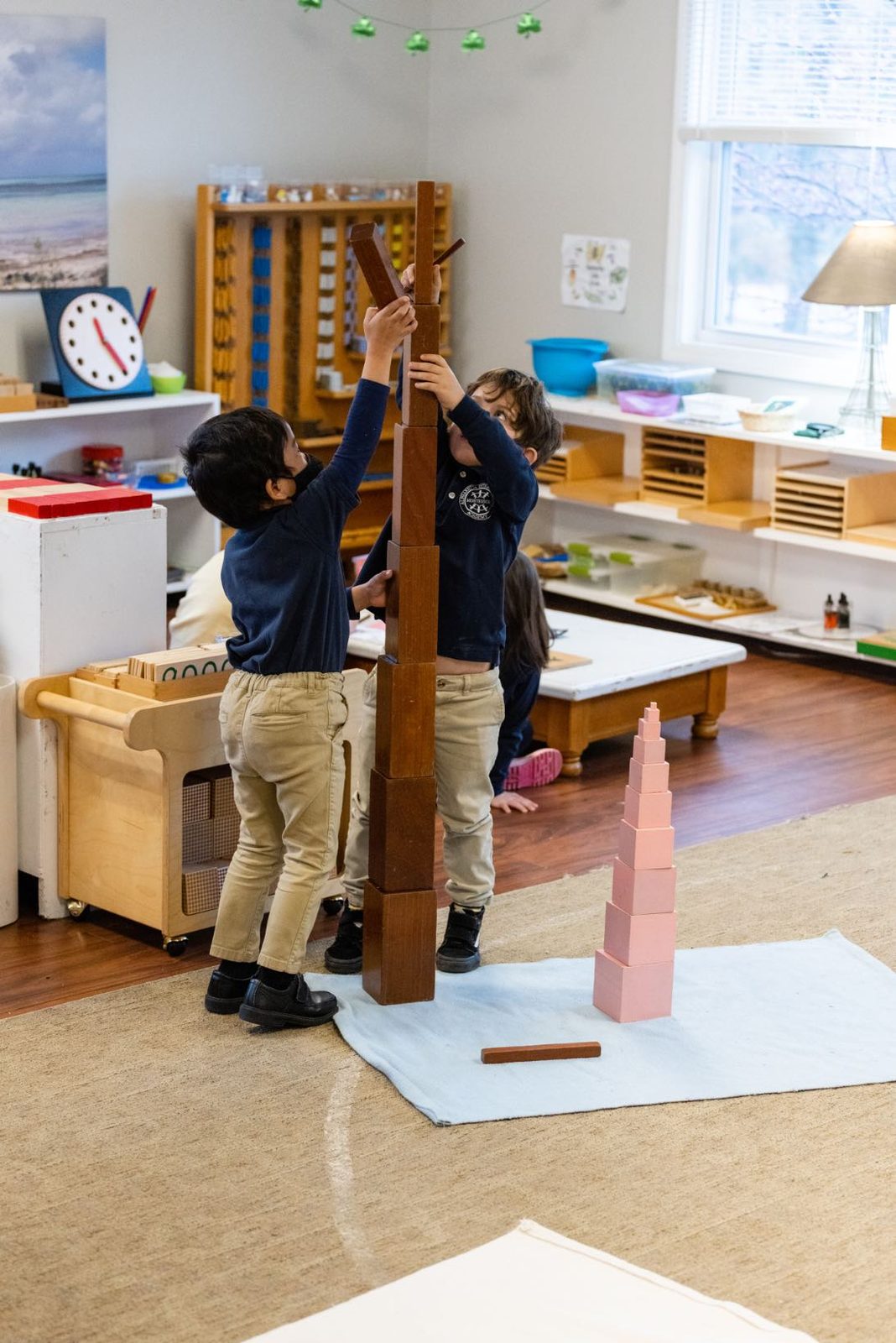 Two AIA students working together to build the brown stair into a tower taller than themselves