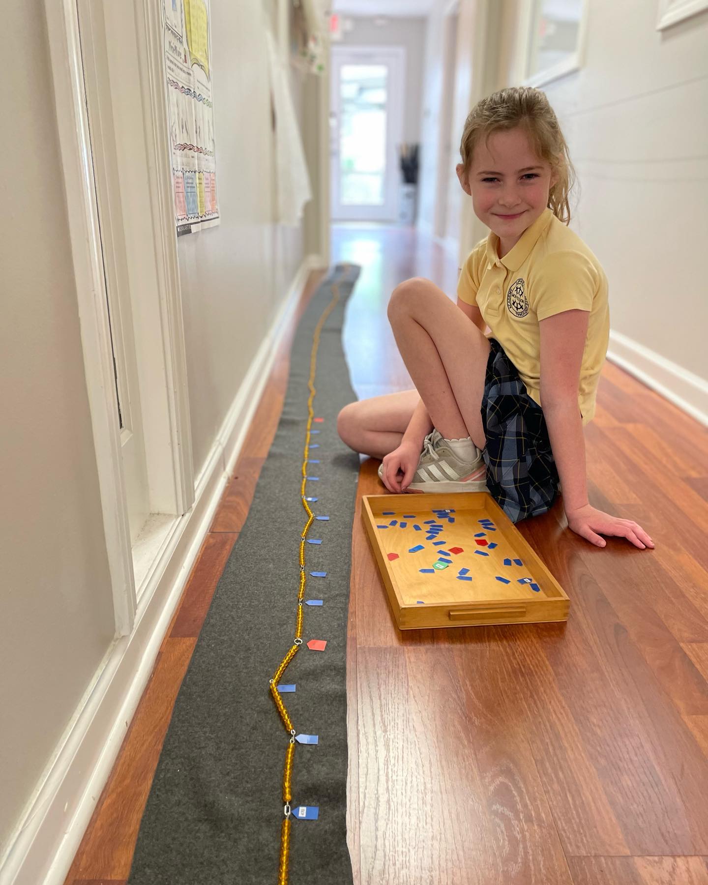 An AIA student skip-counting the Montessori thousand chain of golden beads stretched down the school hallway