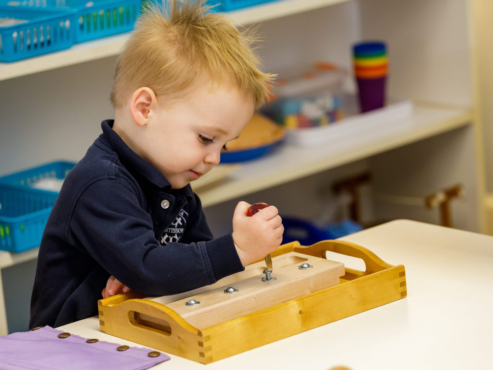 A Pre-Primary toddler concentrating on a practical-life screwdriver work