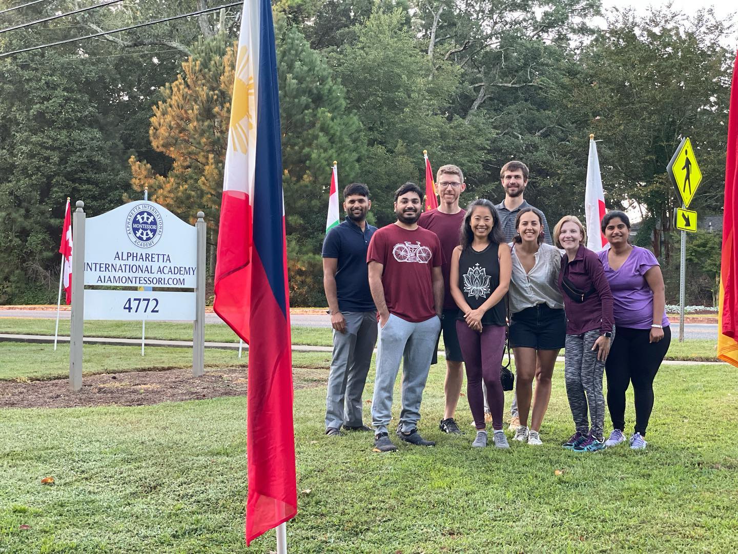 AIA parent volunteers beside the school sign after planting international flags along the road